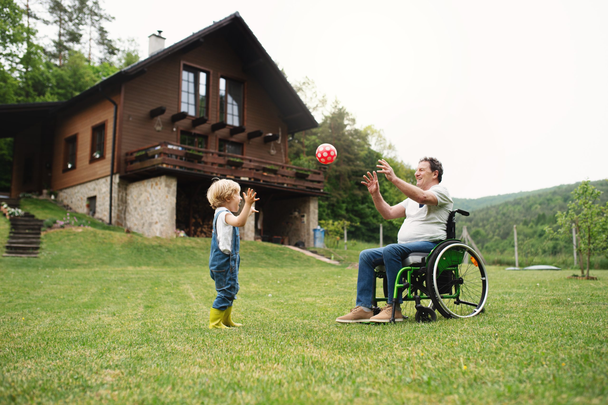 Gilani Mobility Oman Small boy with senior grandfather in wheelchair in garden, playing with a ball.